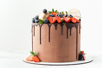 Wall Mural - Birthday cake with milk chocolate frosting decorated with melted dark chocolate drips and fresh summer berries: strawberries and blueberries on top. White background