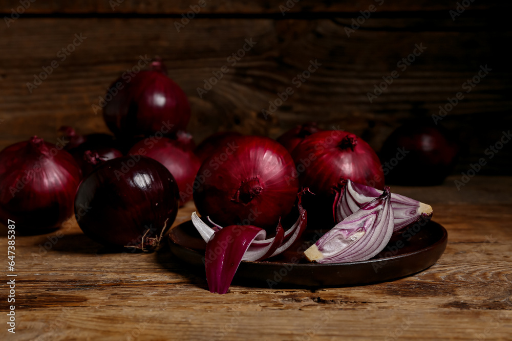 Plate with fresh red onions on wooden background