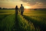 Fototapeta  - Couple holding hands in a green field at sunset