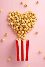 Cinema Bliss: Popcorn Bursting Out Of A Striped Box, Making Heart Shape In A Top-view Vertical Shot Against A Pastel Pink Backdrop, Ready For Text Or Ads