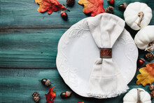 Flat Lay Of A White Plate With Napkin. Place Setting Over A Rustic Wood Table With Colorful Autumn Leaves. Table Top View.  