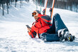 Smiling male skier resting on snow taking a break while using phone. Satisfied confident man wearing red winter jacked and taking ski goggles off lying down on a ski slope and texting on cell phone.