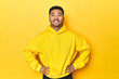 Bold Asian man in yellow hoodie on yellow studio confident keeping hands on hips.