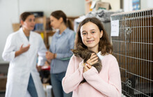 Cheerful Cute Tween Girl Standing Near Cages For Homeless Animals In Shelter, Holding Curious Little Kitten. Pet Adoption And Children Social Responsibility Concept ..