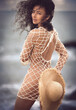 The photo captures  a stunning nude female model, dressed in a Fishnet Mesh  outfit  partly covers her buttocks by a straw hat. The  model, has grey eyes and curly hair, showcases her natural beauty.