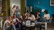 © kinomaster - Medium shot of a group of teens, young people, friends studying, preparing for an exam, discussing, looking at their notes, using devices, watching something.