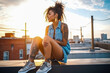 Photo of a young african american female millennial on a rooftop, showcasing her tattoos and wearing denim cutoff shorts. With trendy style and urban vibe reflect a carefree and confident spirit