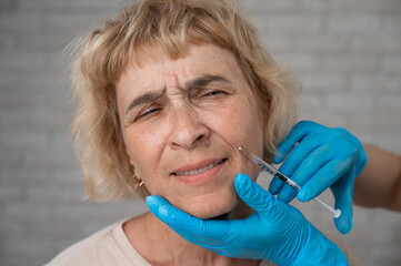 Wall Mural - Doctor makes beauty injections in the face of an old caucasian woman. 