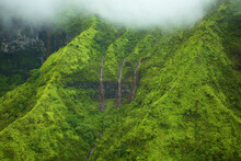 Waterfalls Flowing Through Lush Green Hills Under The Low Lying Clouds; Hawaii United States Of America