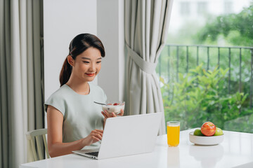 Wall Mural - Beautiful young woman working on laptop while sitting at breakfast table in morning.