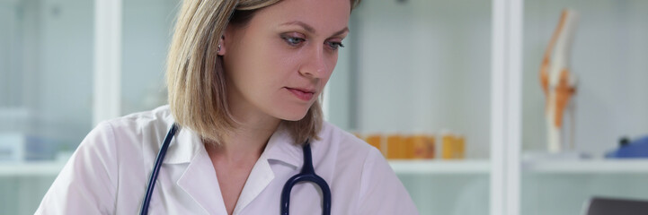 Wall Mural - Female doctor holds clipboard with documents and works at computer in medical office.