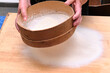 Donna setaccia della farina su tavolo di legno