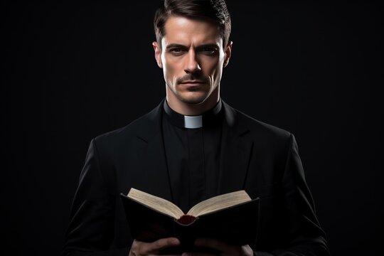 Catholic christian church priest wearing black cassock robe holding the holy bible book in his hands. Isolated on dark black background.