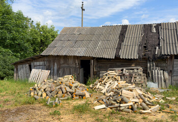 Wall Mural - Pile of chopped firewood in village near house. Chopping wood and cutting timber. Preparation of firewood in village for heating house in winter. Old barn in countryside. Rural landscape.