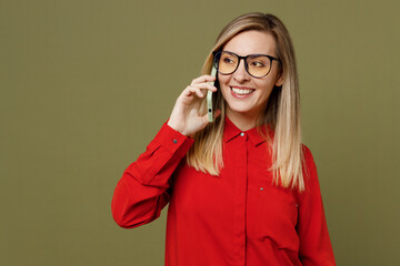 Wall Mural - Young woman she wearing red shirt casual clothes glasses talk speak on mobile cell phone conducting pleasant conversation isolated on plain pastel green background studio portrait. Lifestyle concept.