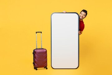 Wall Mural - Traveler Indian man hold big huge blank screen mobile cell phone bag walk isolated on plain yellow background. Tourist travel abroad in free spare time rest getaway. Air flight trip journey concept.