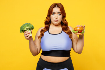 Wall Mural - Young sad chubby overweight plus size big fat fit woman wear blue top warm up train hold choose between broccoli and burger isolated on plain yellow background studio home gym. Workout sport concept.