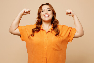 Wall Mural - Young ginger chubby overweight woman she wear orange shirt casual clothes show biceps muscles on hand demonstrating strength power isolated on plain beige background studio portrait Lifestyle concept