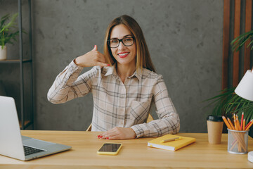 Wall Mural - Young cheerful successful employee business woman wear shirt casual clothes glasses sit work at office desk with pc laptop, doing phone gesture like says call me back. Achievement career job concept.