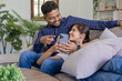 © Wuttichaik - Smiling couple embracing while looking at mobile phone, Loving couple relaxing on sofa