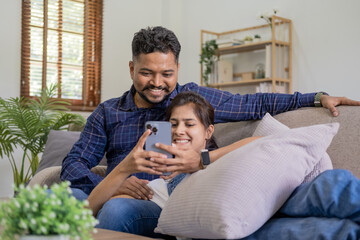 Smiling couple embracing while looking at mobile phone, Loving couple relaxing on sofa