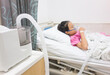 Ill young Asian girl sleeping on bed in hospital. Sick kid with Medical ultrasonic inhaler, nebulizer, nebular with mask. Respiratory medicine. Asthma breathing treatment. Asthmatic health equipment.