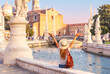 Happy female tourist with arms raised sitting on prato della valle square during sunset- Padua in Italy