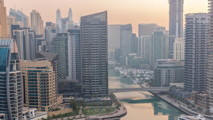 Wall Mural - Dubai Marina with several boats and yachts parked in harbor and skyscrapers around canal aerial night to day timelapse.