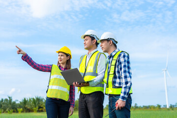 Wall Mural - Team of 3 male and female engineers, Asian professionals Wear a safety helmet and vest. point to destination There are radios and tablets for industrial work, and there is a wind turbine.