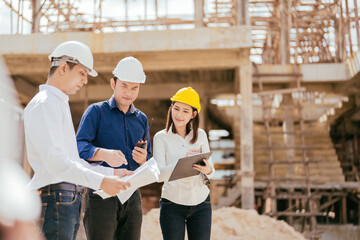 Wall Mural - Construction project has a team of 3 male and female engineers, Asians, looking at architectural industrial site design blueprints, with radios, list notes, wearing hard hats and uniforms.