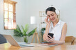 © Natee Meepian - Women asian sitting on desk and wearing headphone to listen music on smartphone in lifestyle at home