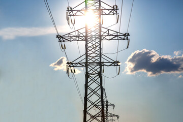 The concept of a source of electricity. Energy industry. High voltage tower with power wires against the background of the sun and clouds.