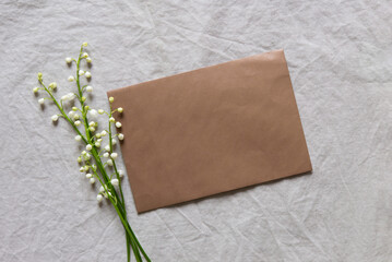 Poster - Blank greeting card, invitation and envelope mockup. Minimal floral arrangement with white lilies of the valley. Flat lay, top view. Happy mother's day, birthday, wedding composition.