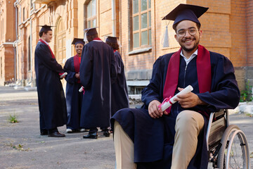 Portrait of student with disability sitting on wheelchair and smiling at camera, he graduating from university