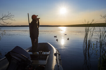 Wall Mural - hunter standing it boat and blowing at hunter's whistle. duck hunter at sunrise.