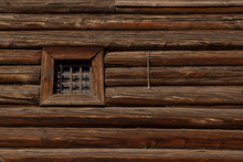 The Wall Of An Old Log House With A Small Window Behind Bars