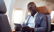 © Andrii IURLOV - Smiling happy black businessman flying and working in an airplane in first class, Man  sitting inside an airplane using laptop.