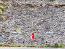 A Red Post Box In The Middle Of A Large Stone Wall In A Village In England