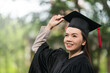 © EduLife Photos - Adult female Asian student in academic gown and graduation hat standing outside college.