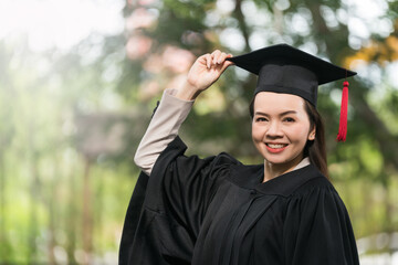 Wall Mural - Adult female Asian student in academic gown and graduation hat standing outside college.