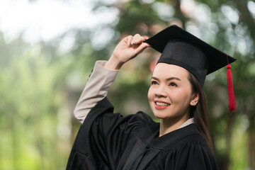 Wall Mural - Adult female Asian student in academic gown and graduation hat standing outside college.