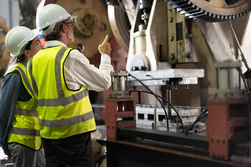 Senior manager on job training female technician working in metal sheet production factory. Skill engineer and team standing in manufacturing facility talking machinery maintenance in heavy mechanic