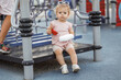 Adorable toddler with a broken arm of a child in a cast sitting on the playground. Girl a 2-3-year-old keeps her arm bent against the background of a pink T-shirt. Trauma after visiting the playground