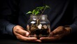 Businessman hands holding a glass container full of coins and little plant