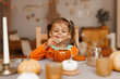 Happy Halloween! Little cute girl eating cookies in the kitchen. Toddler girl in a pumpkin costume eating sandwiches on breakfast. Morning at home.