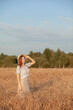 © Anat art - A young beautiful girl with braces on her teeth and long hair poses in a wheat field in the summer at sunset. The girl holds a hat in her hand against the background of a wheat field.