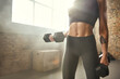 © Friends Stock - Close-up of young athletic woman with tattoo on her hand in sportswear exercising with dumbbells while standing in front of window at gym.