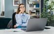 © MYDAYcontent - Young thoughtful woman wearing eyeglasses dreaming at desk with laptop, motivated idea concept, working in cozy light room