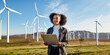 © Davis Brown - Young Black Woman Standing in Field with Wind Turbines for Renewable Energy - Ideal for Environmental and Sustainability Content, Generated by AI