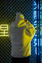 Canvas Print - A woman with curly hair in a white hat and hoodie stands against the background of neon signs.